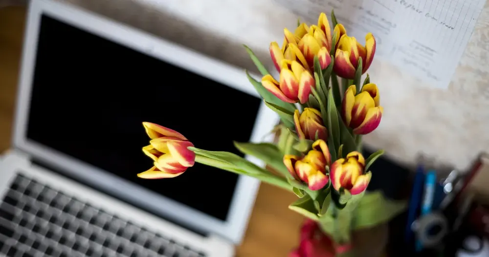 Notebook aberto sobre mesa ao lado de vaso com tulipas